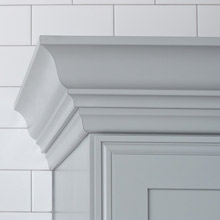 light gray crown moulding mounted to top of cabinet in matching finish against a white-tiled wall