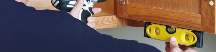 man using a power drill and small level to accurately adjust a cabinet door